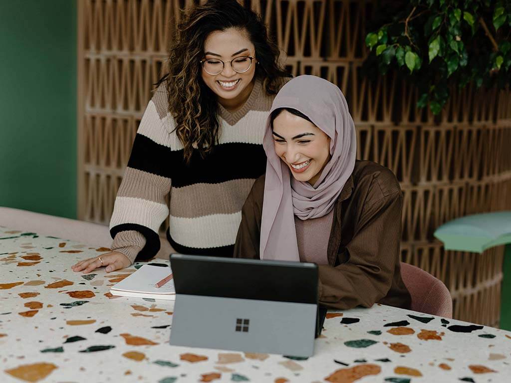 Women laughing while working at laptop